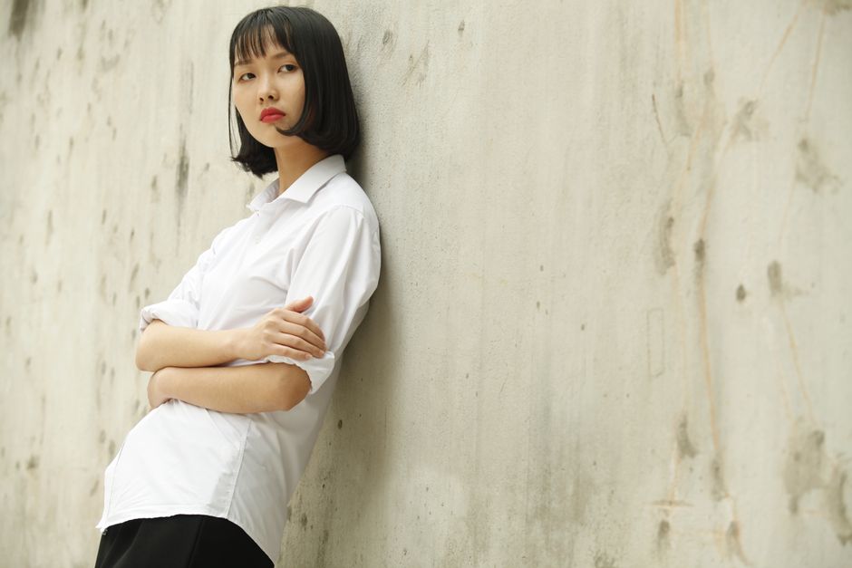 Chic young woman in white shirt posing against a textured wall, embodying modern fashion.
