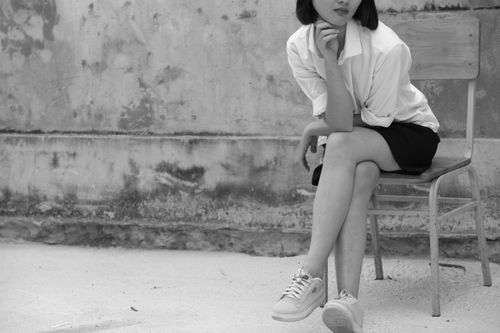 Free Black and white photo of a woman sitting on a chair outdoors, showcasing fashion and elegance. Stock Photo
