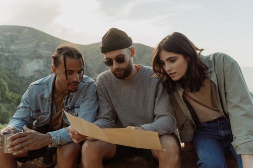 Free Three young adults studying a map while hiking in the mountains on a sunny day. Stock Photo
