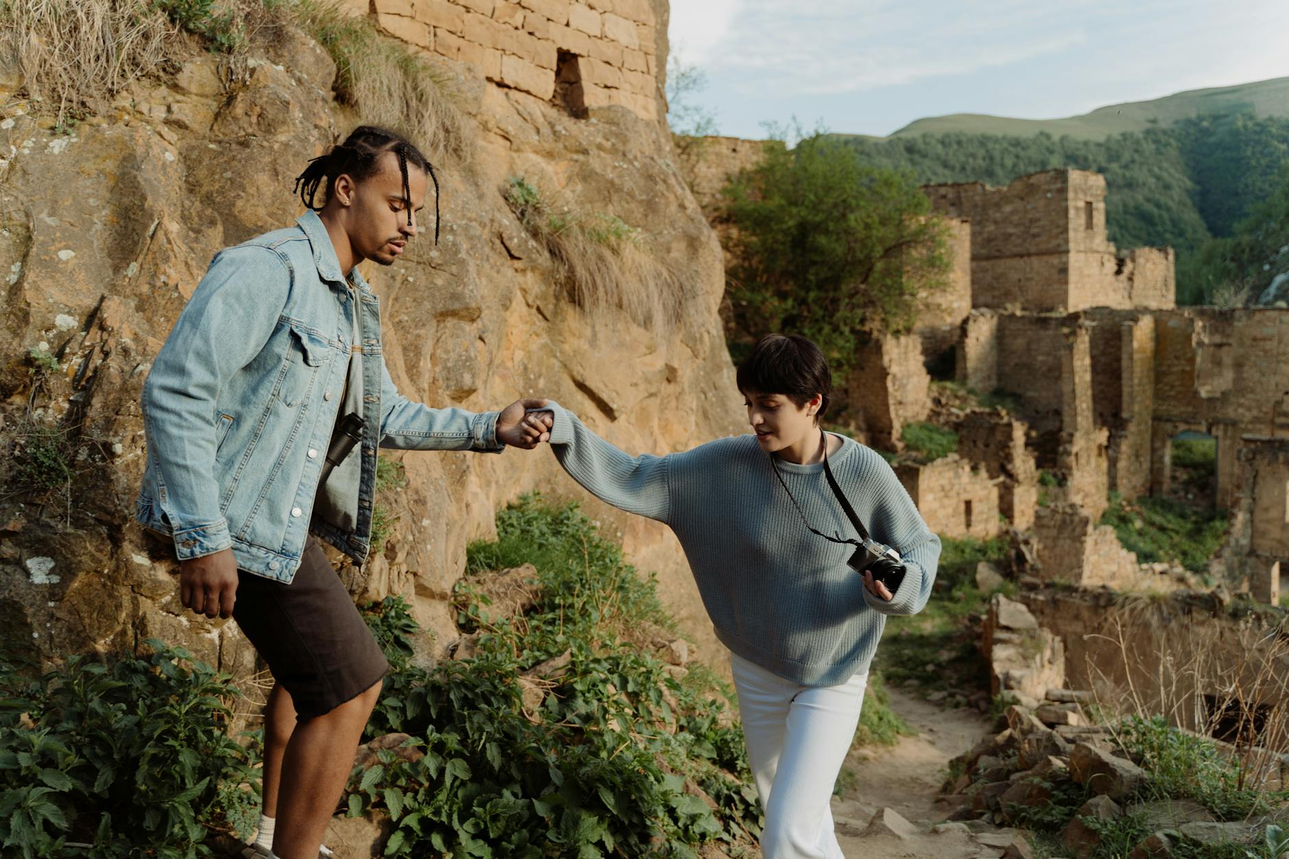 A couple hiking and helping each other at ancient ruins in the Caucasus mountains.