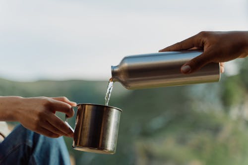 Person Pouring Water on Stainless Steel Mug 