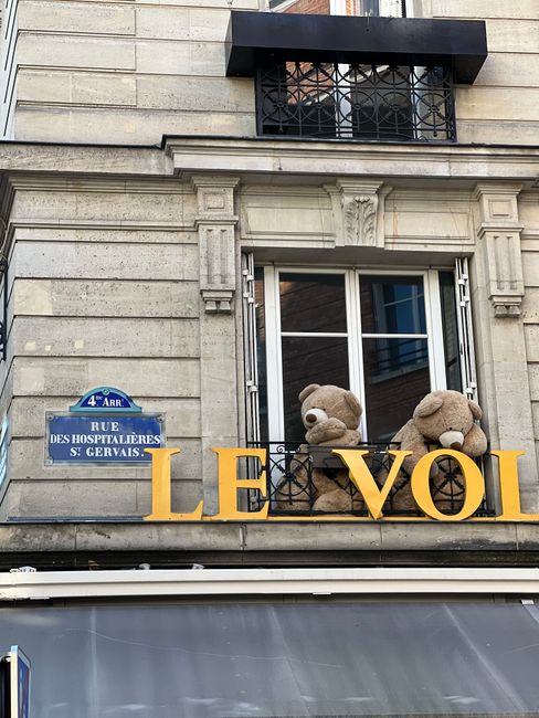 Two plush teddy bears sit on a historic balcony in Paris, France.