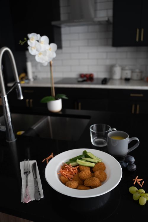 Free Stylish kitchen with a meal of nuggets, cucumber, and carrots on a black countertop. Stock Photo