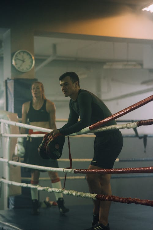 A Man and a Woman Resting in a Boxing Ring After a Spar