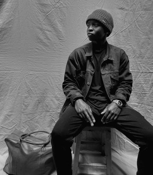 Grayscale Photo of Young Man Wearing Jacket Sitting on Chair