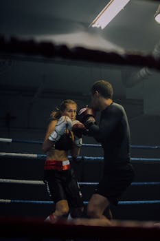 A man and woman spar vigorously in a boxing ring, showcasing athletic strength.