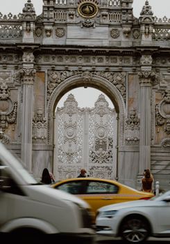 Intricate architecture of Dolmabahçe Palace entrance with bustling city traffic in Istanbul.