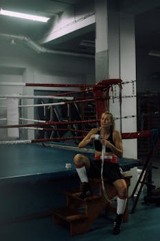 Female boxer sitting by the ring wrapping hands, preparing for training.