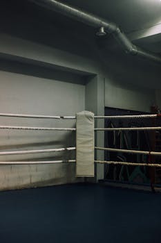 A dimly lit boxing ring in an indoor gym showcasing an industrial atmosphere.