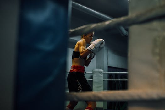 Focused female boxer practicing in an indoor boxing ring, wearing gloves and athletic attire.