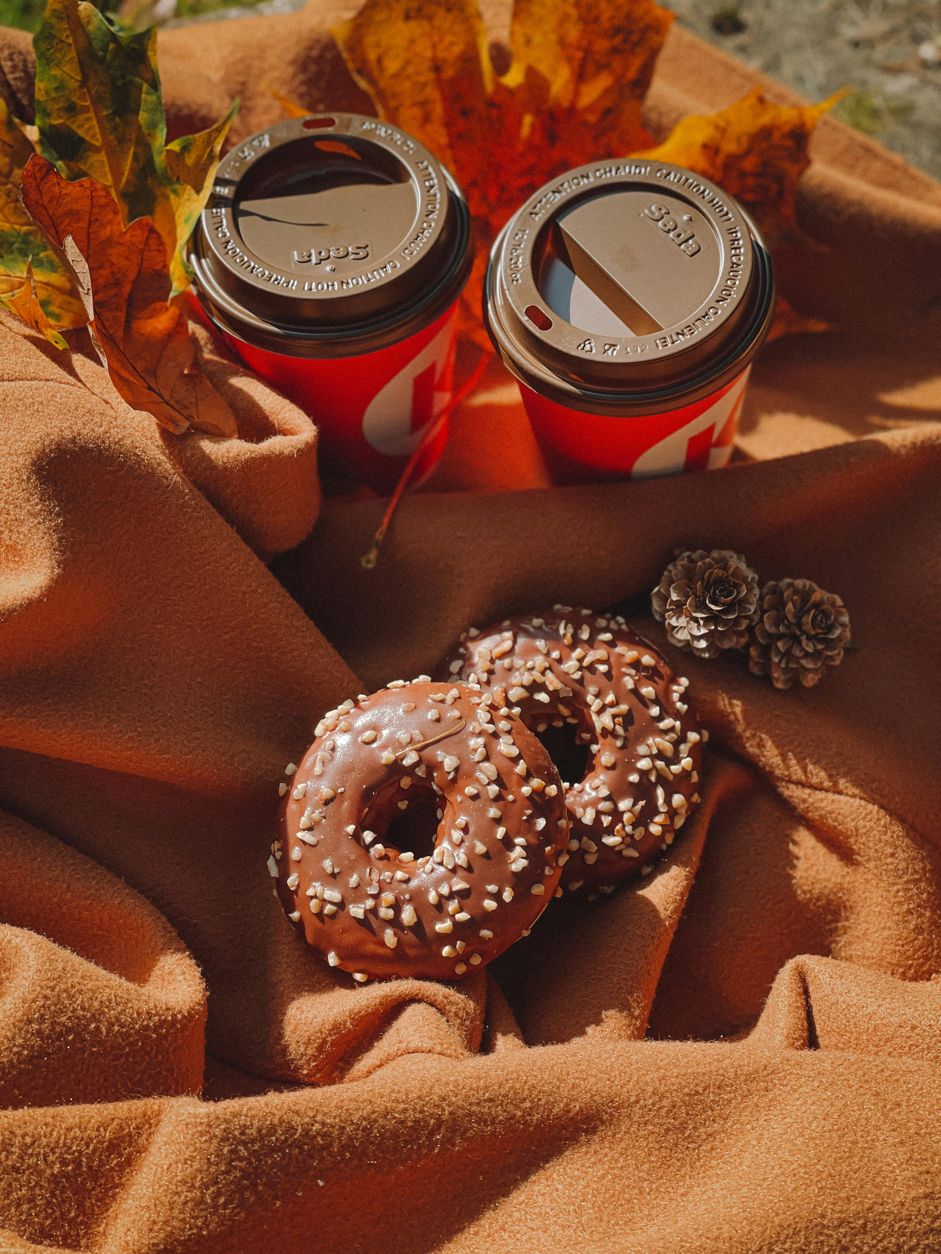 Cozy autumn scene with coffee cups and chocolate donuts on a warm orange blanket.