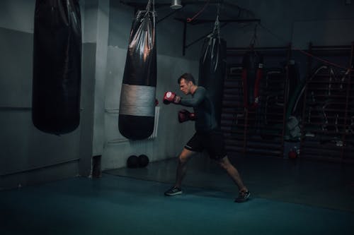 A Man in Grey Compression Shirt Punching a Black Punching Bag