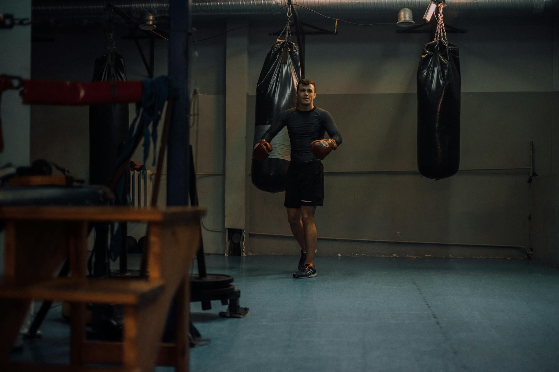 A Man in Grey Compression Shirt Standing in Front of the Black Punching Bags