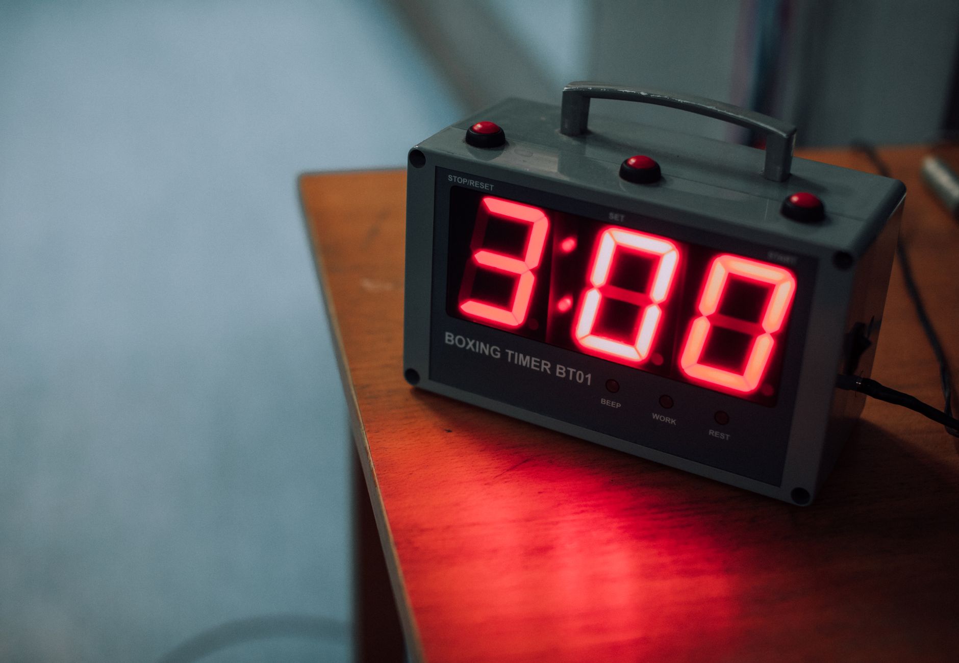 A digital boxing timer displaying 3:00 resting on a wooden table.