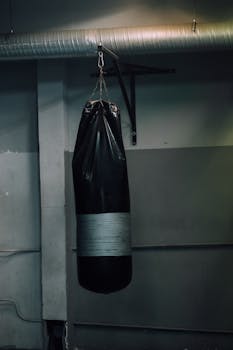 A black heavy-duty punching bag hanging in an indoor training gym.