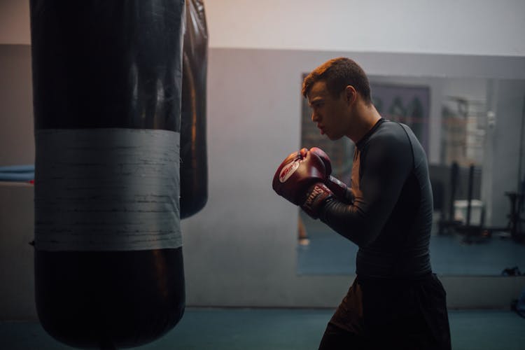 A Side View Of A Man Wearing Boxing Gloves While Facing A Punching Bag