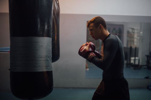 Free Young male boxer in black attire training with a punching bag indoors. Stock Photo