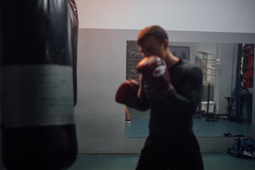 A boxer in black attire trains intensely with a punching bag in a gym.