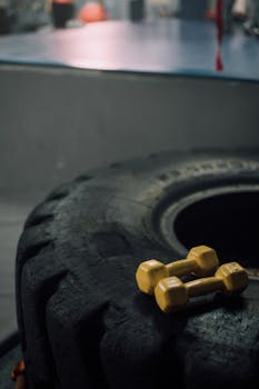 Close-up of a large tire with yellow dumbbells in a gym setting, emphasizing strength training.