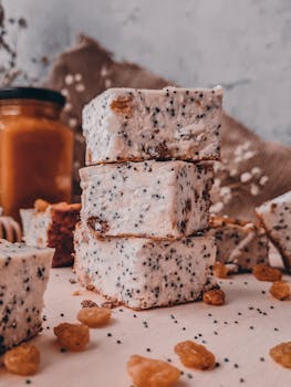 Stacked poppy seed pastries on rustic surface with raisins and honey jar in background.