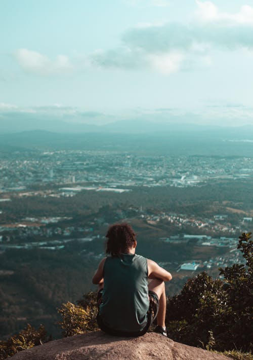 A Person in Gray T-shirt Sitting on Rock Looking at the City