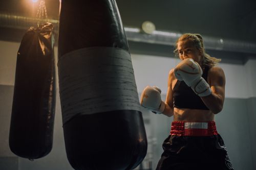 Free Fierce female boxer honing her skills in a gym, delivering powerful punches to a heavy bag. Stock Photo
