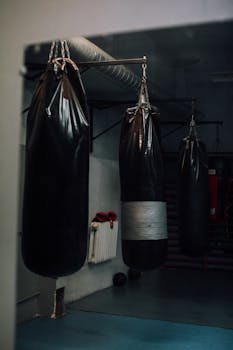 Atmospheric gym interior with hanging punching bags and shadowy lighting.