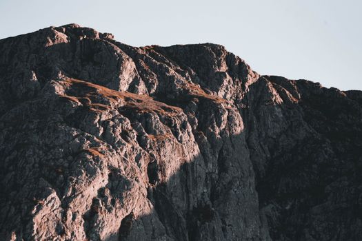 Dramatic mountain cliff showcasing intricate rock formations during sunset.