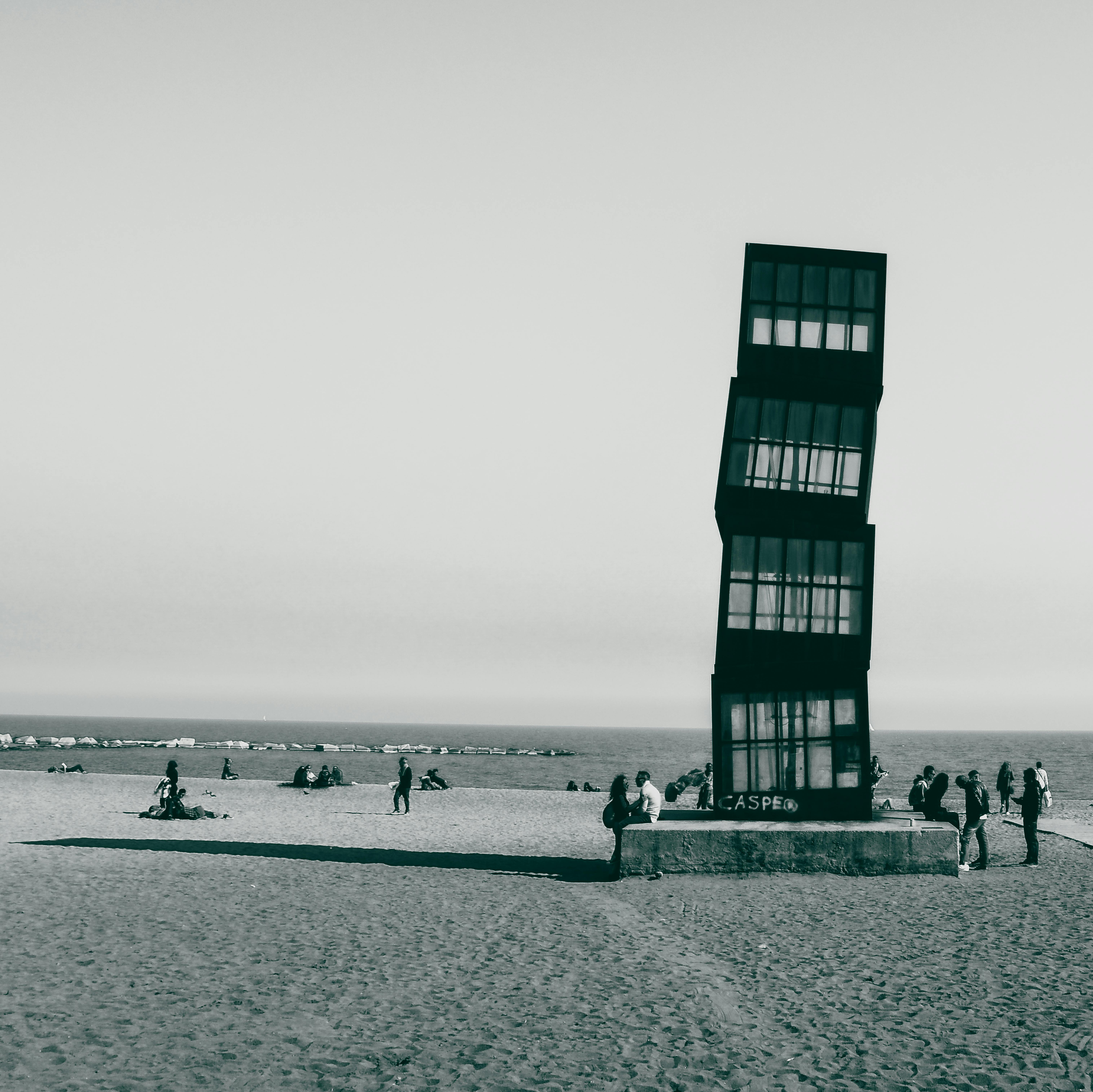 a grayscale photo of people on the beach near the famous landmark
