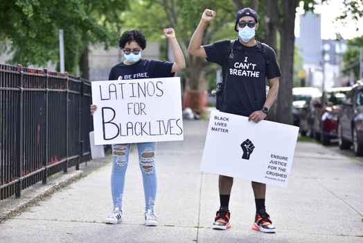 Two protesters stand on the sidewalk holding signs advocating for Black Lives Matter and racial equality.
