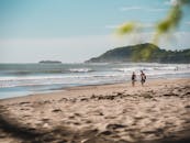 两名成年人在尼加拉瓜马塔加尔帕的沙滩上，沿着海浪和丘陵行走