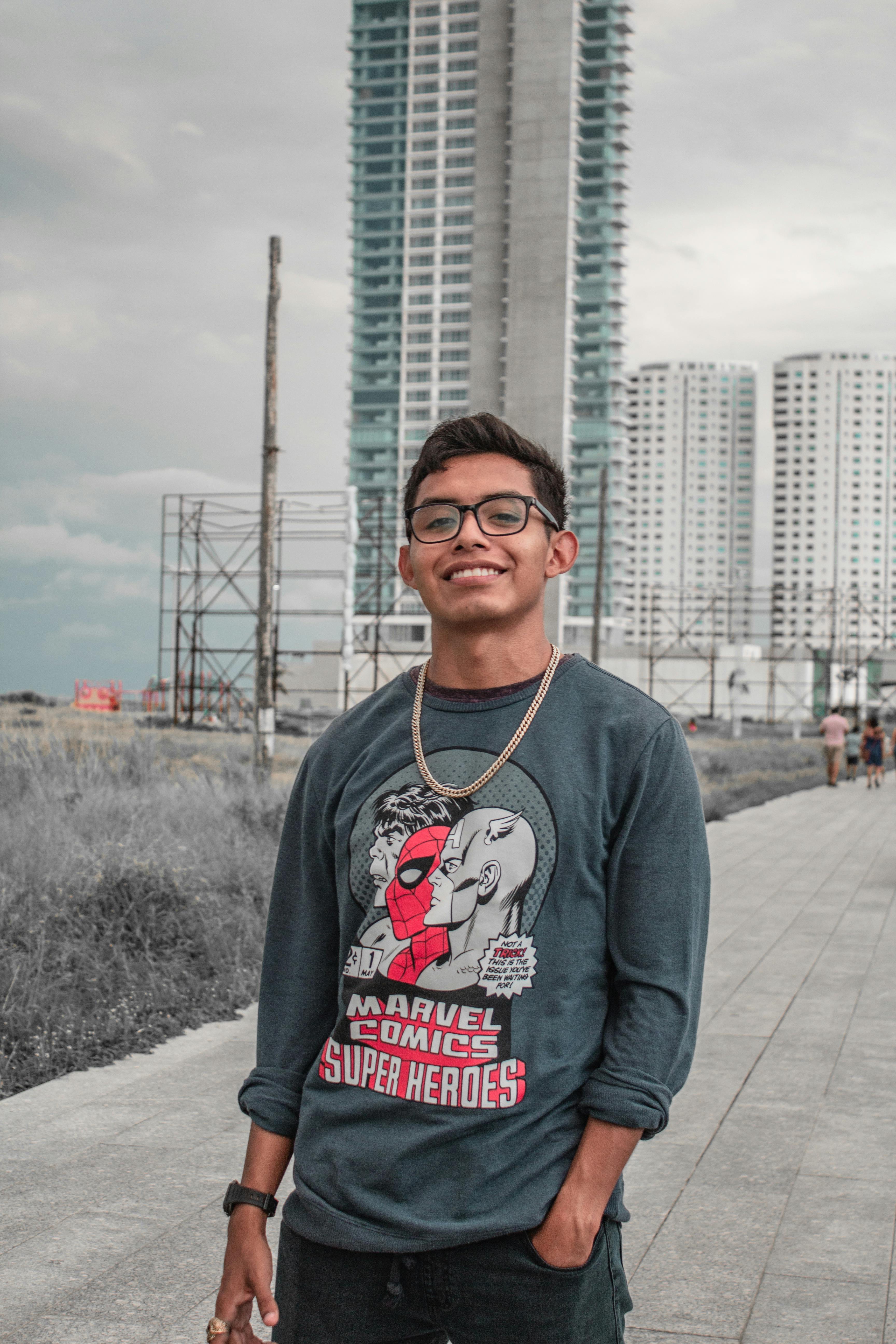 Young man smiling in front of urban skyscrapers wearing a Marvel Comics sweatshirt.