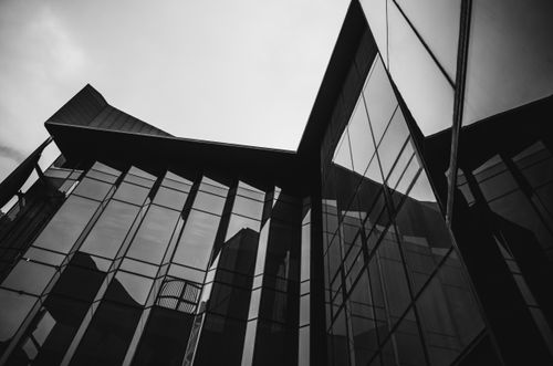 Free Low-angle black and white photo capturing a modern glass building's dramatic lines and reflections. Stock Photo