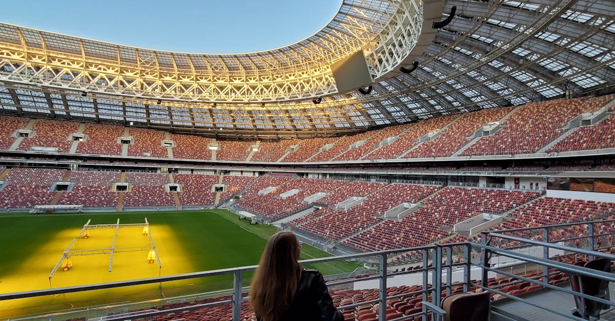 Photo by Rockwell branding agency A solitary person sitting in a sunlit football stadium, offering a sense of quiet amidst the vast architecture.