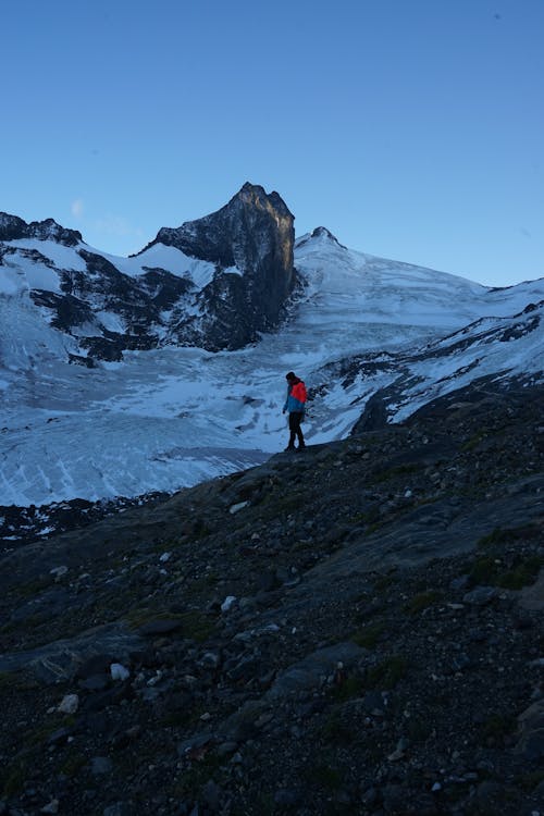 Person in Red Jacket and Black Pants Standing on Rocky Mountain