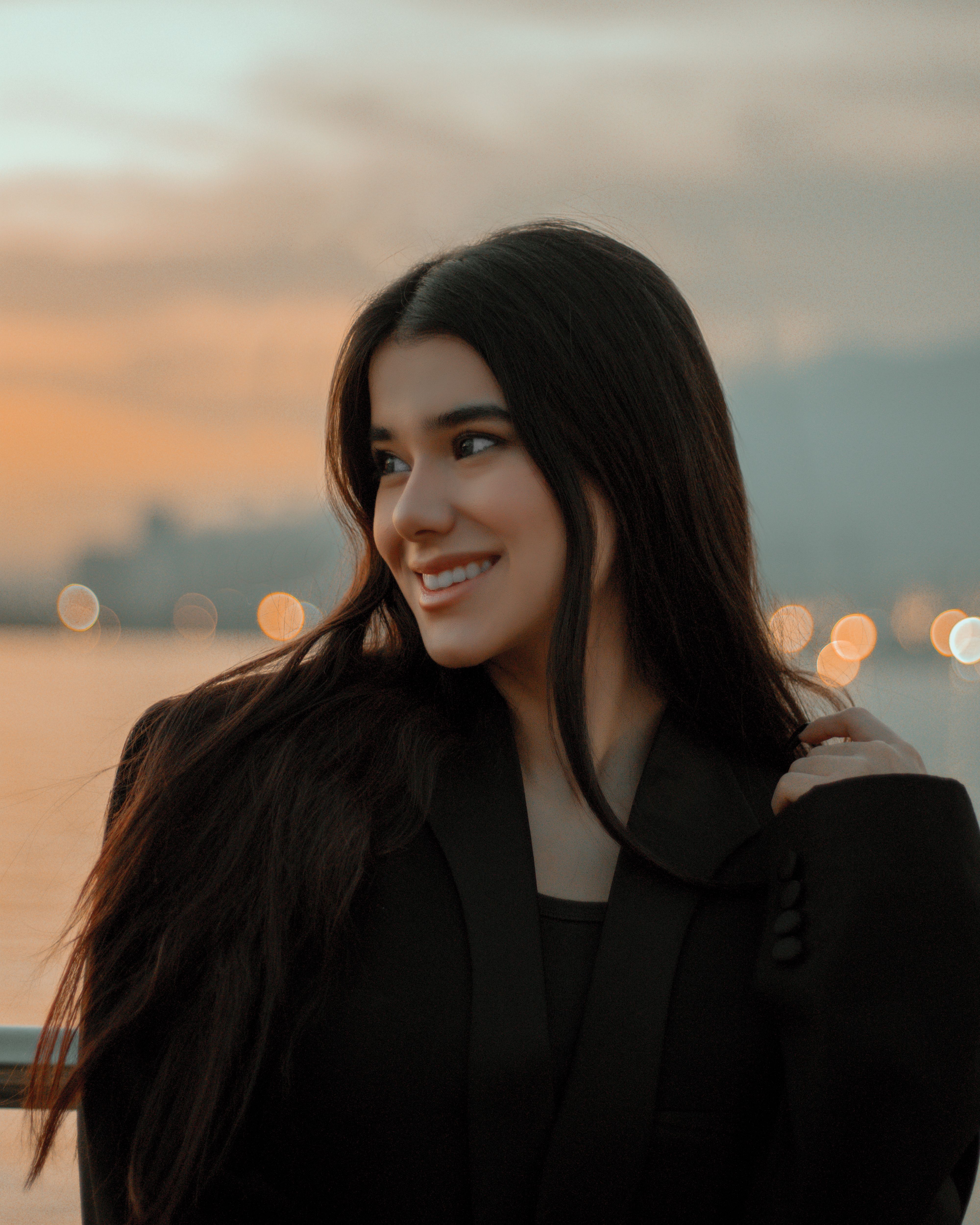 Portrait of a smiling woman with flowing hair at sunset near the water.