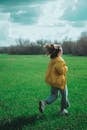 Woman in Yellow Coat Running Across Grass Field