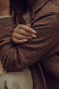 Close-up of a woman's hand with manicured nails resting on a checkered blazer.