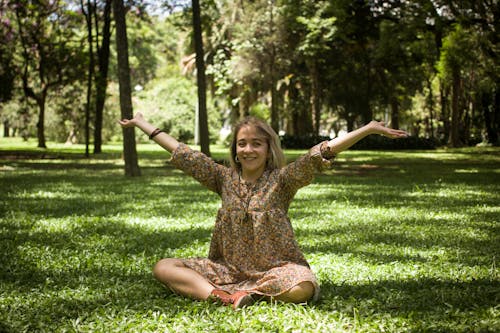 Photo of a Woman Sitting on Green Grass while Raising Her Arms