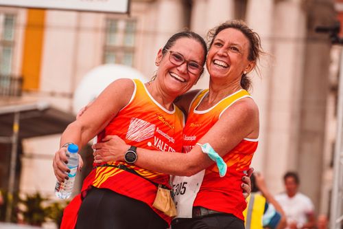 Free Two women joyfully embrace after finishing a marathon in a vibrant city setting. Stock Photo