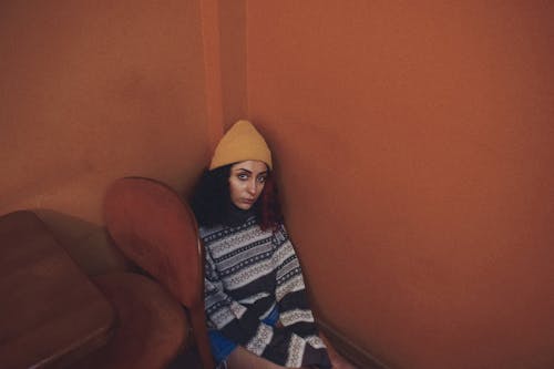 Woman in Winter Hat and Sweater Sitting on Floor in Corner of Room