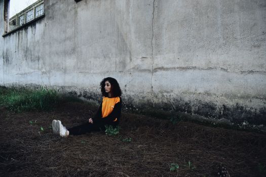 Young Woman Sitting Lonely on Ground under Dingy Wall of Industrial Building