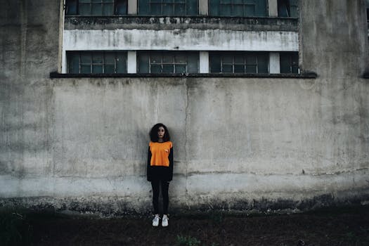 Young woman in orange outfit standing against a concrete wall of an industrial building.