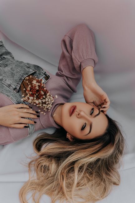 A woman with dyed wavy hair and flowers rests indoors, exuding beauty and calm.