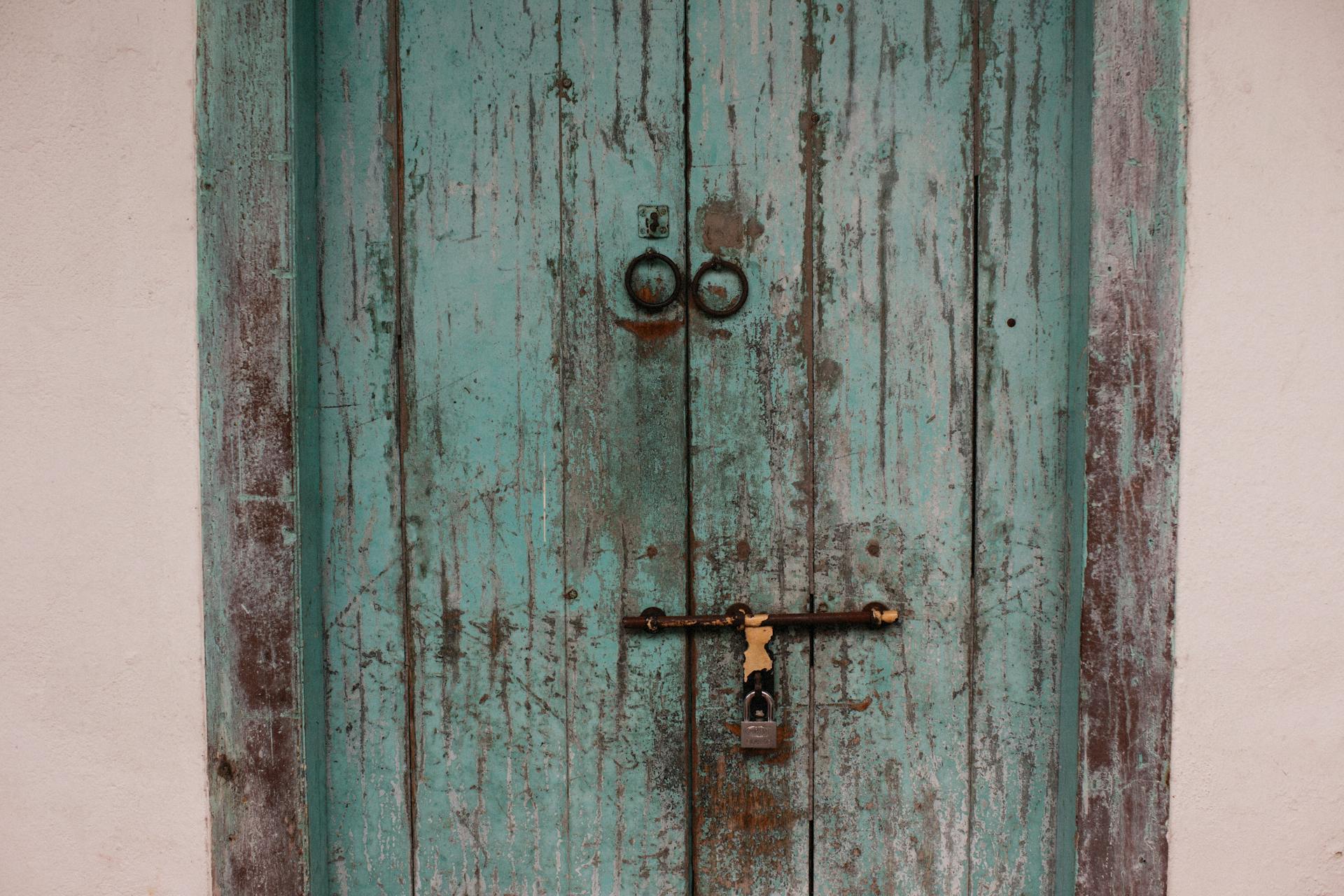 Weathered turquoise wooden door with a padlock, symbolizing security and history.