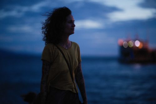 Free Silhouette of a woman gazing at the sea during twilight with a ship in the distance. Stock Photo