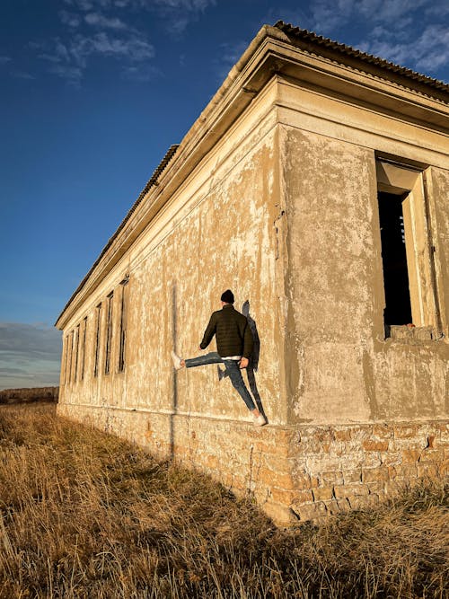 Man Standing on One Leg on the Side of Abondoned Building