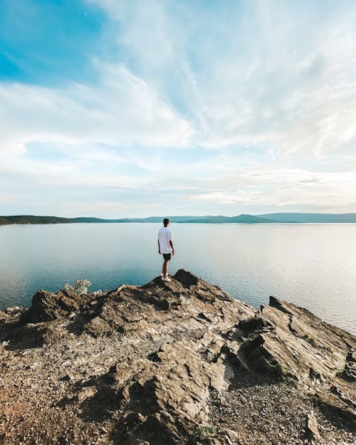 Man Standing at the Edge of Rock Formation Next to Lake
