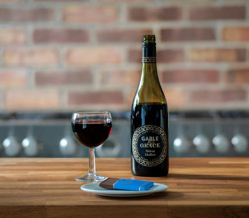 Wine Bottle Beside A Glass Of Red Wine on Wooden Table