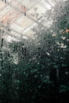 A close-up shot of a moist glass surface revealing a blurred view of nature behind it.